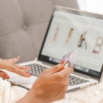 A woman relaxes on a couch while shopping online using her laptop and credit card.